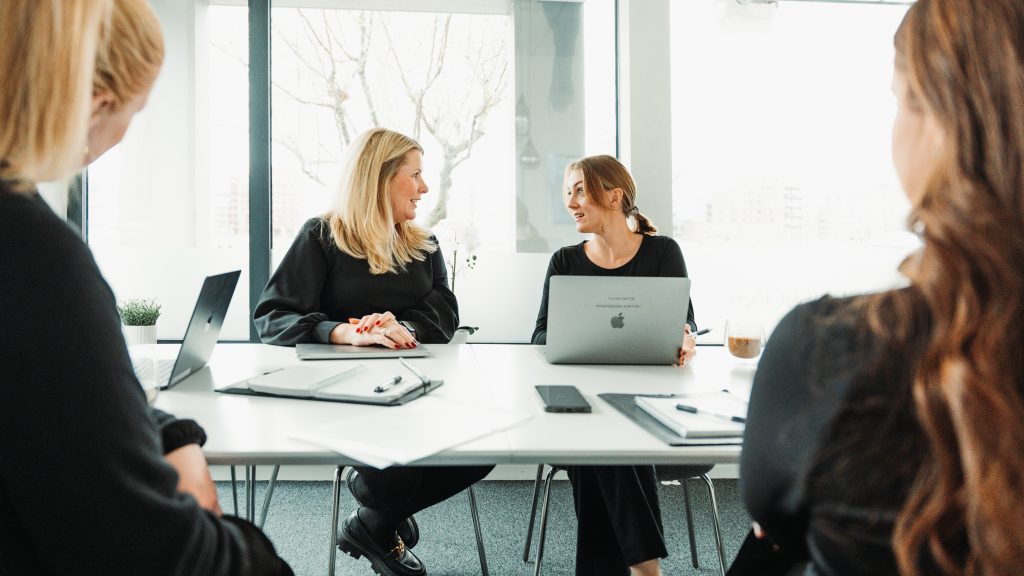 Fyra kollegor i möte på kontor – diskuterar bemanning och rekrytering vid konferensbord med laptops